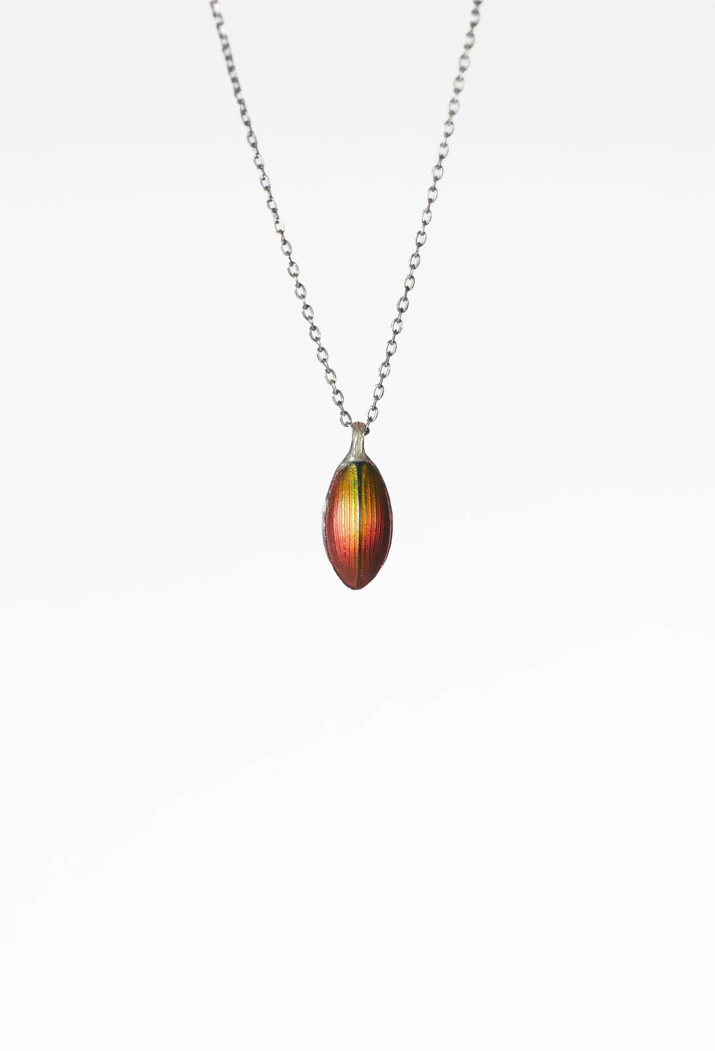 A Chitiner - Red Seed Necklace  
Oval-shaped multicolored pendant, mainly red and green  
Subtle vertical stripes, nature-inspired jewelry