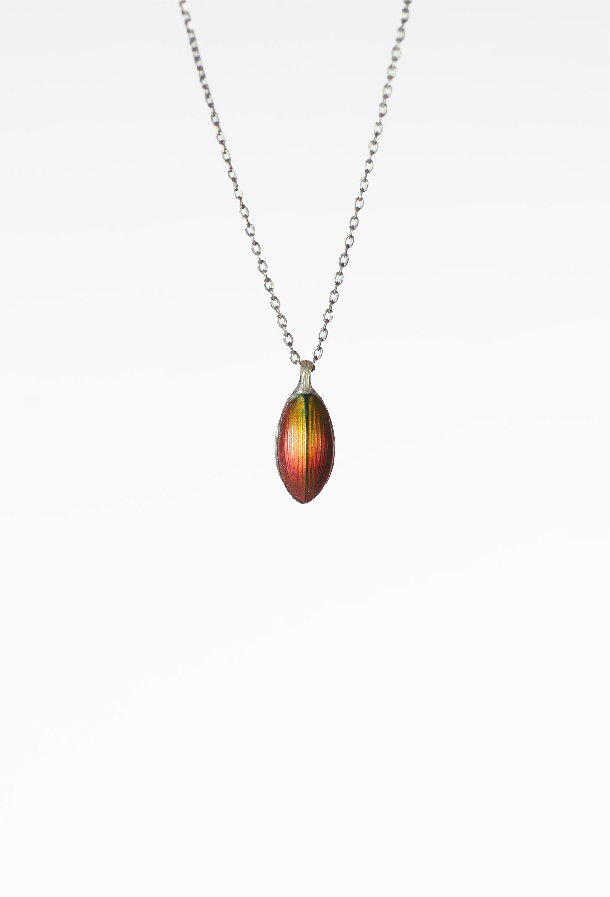 A Chitiner - Red Seed Necklace  
Oval-shaped multicolored pendant, mainly red and green  
Subtle vertical stripes, nature-inspired jewelry